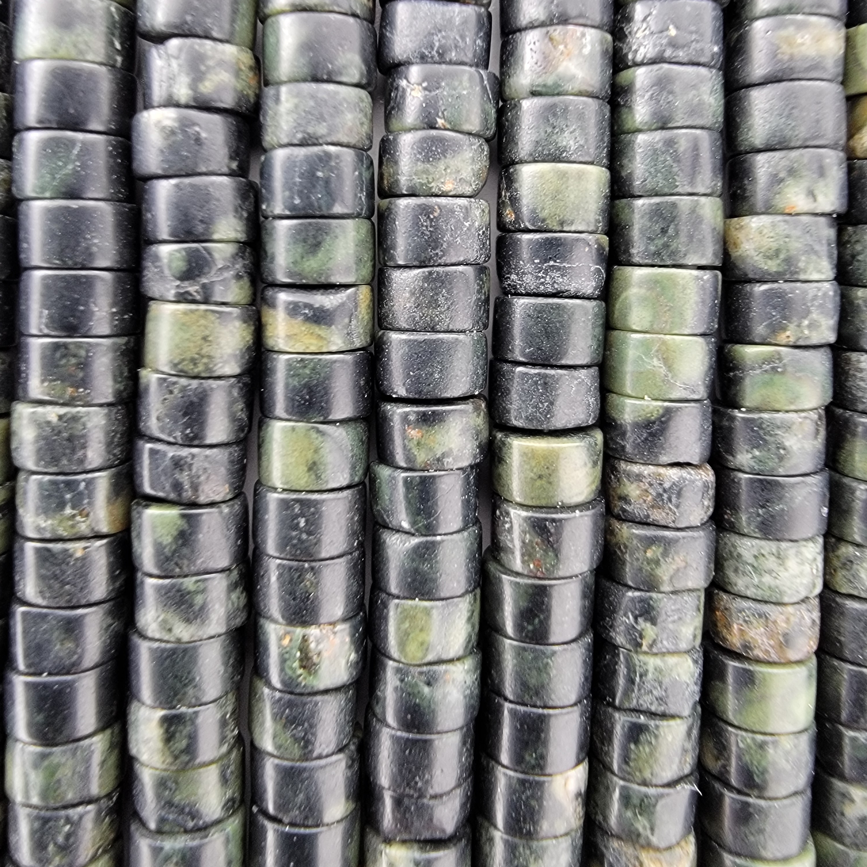 Close-up of multiple vertical strands of polished rectangular beads in a green and black stone with natural green marbling.